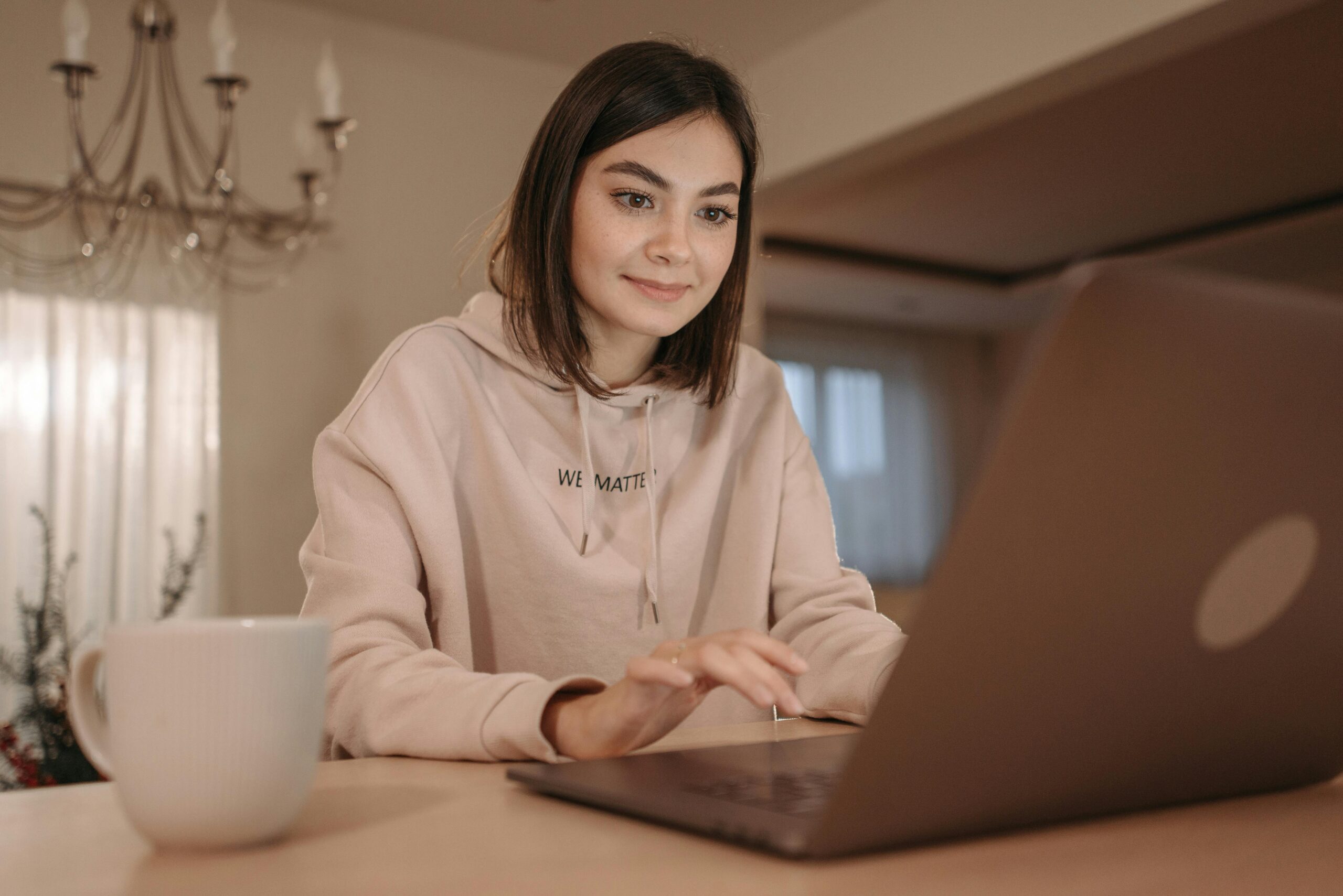 A young woman in a cozy setting using a laptop with a cup of coffee nearby.